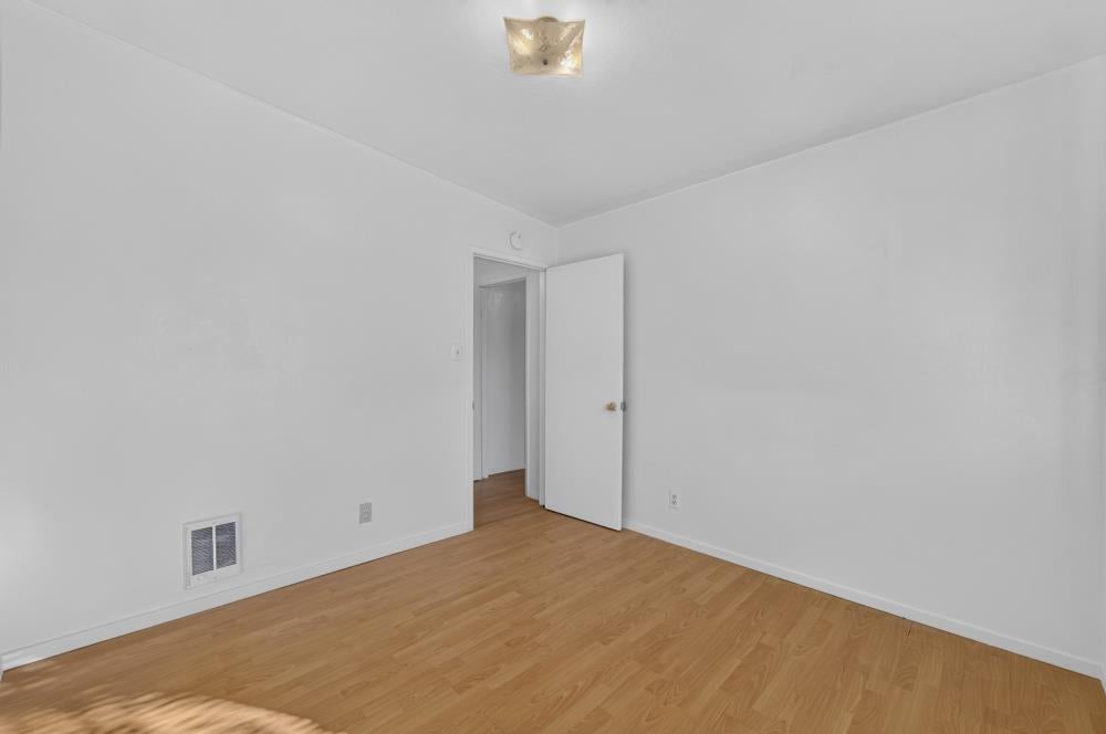 Empty room with light wood flooring, white walls, and an open doorway.
