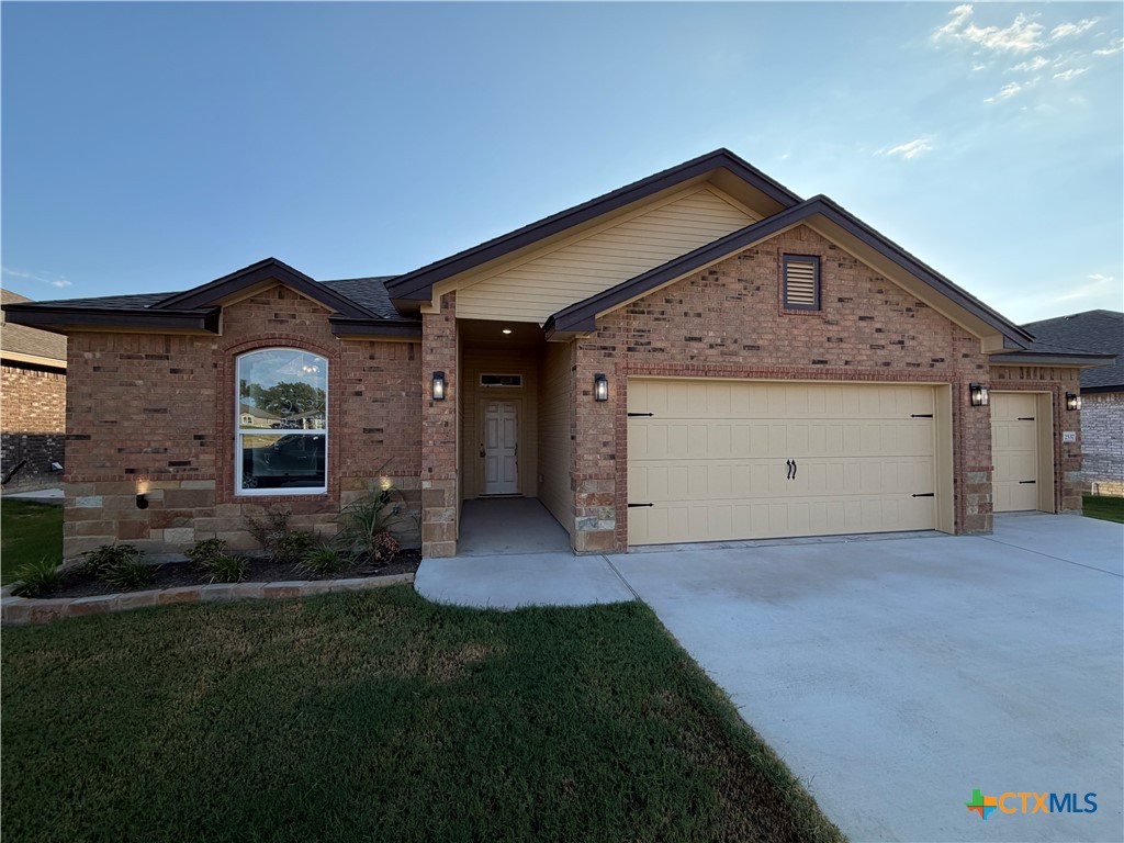Brick home with stone accents, covered entry, two-car garage, and front lawn