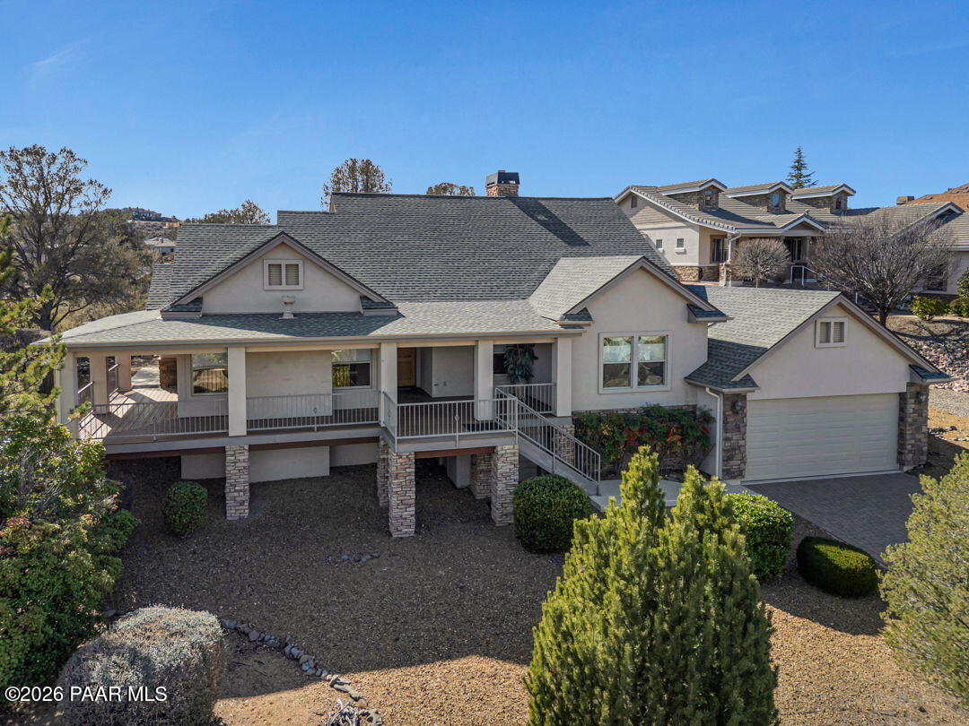 Stucco home with a broad covered porch, raised stone supports, attached garage, and landscaped yard.