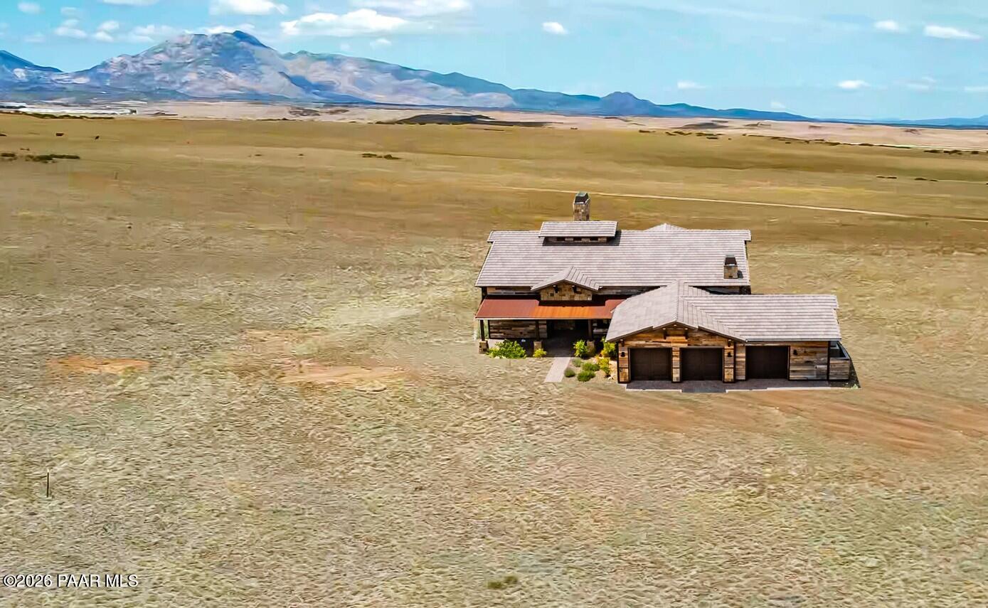 Aerial view of a ranch-style home with three-car garage on open grassland beneath distant mountains.