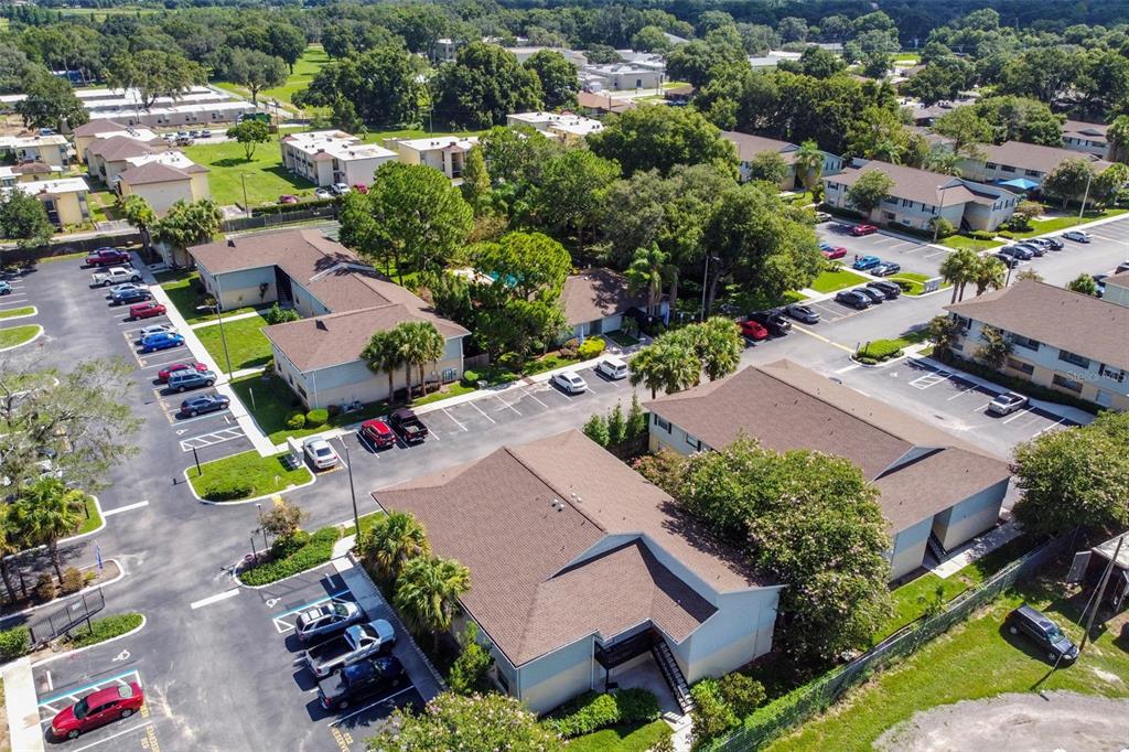 Aerial view of a condominium community with parking lots, mature trees, and landscaped grounds.