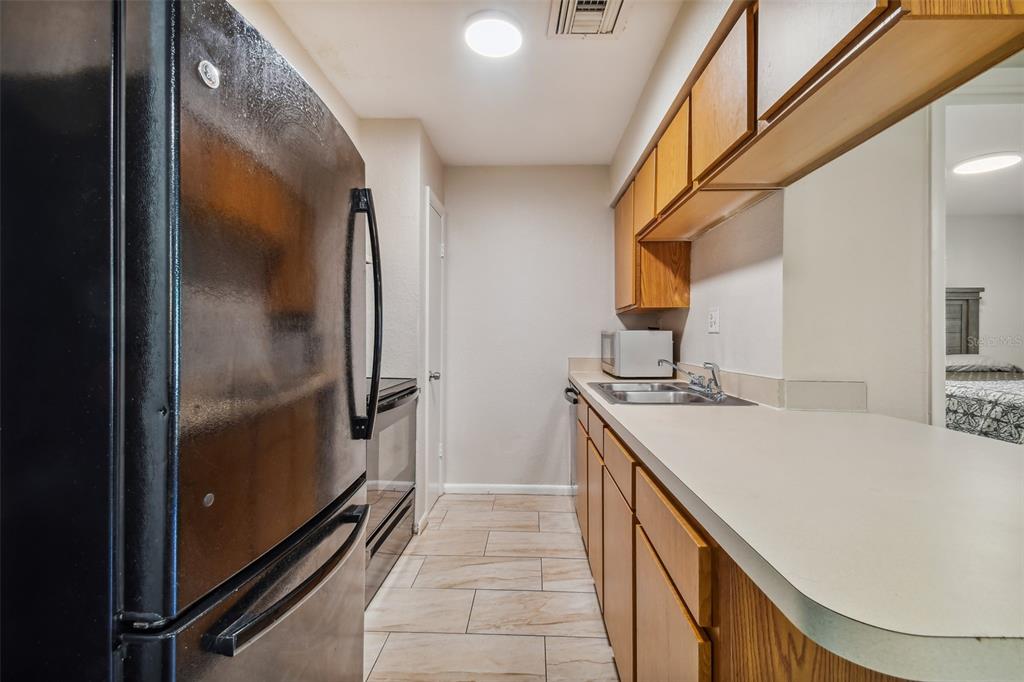 Galley kitchen with warm wood cabinets, a long countertop, stainless steel appliances, and beige tile flooring.