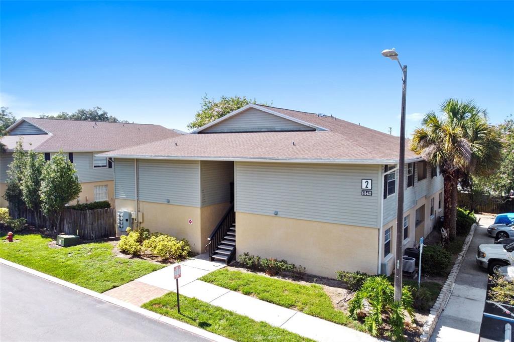 Two-story condominium building with pale blue siding, a central staircase, and a palm tree beside the parking area.