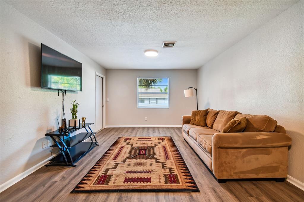 Living room with a tan sofa, patterned rug, and wall-mounted television.