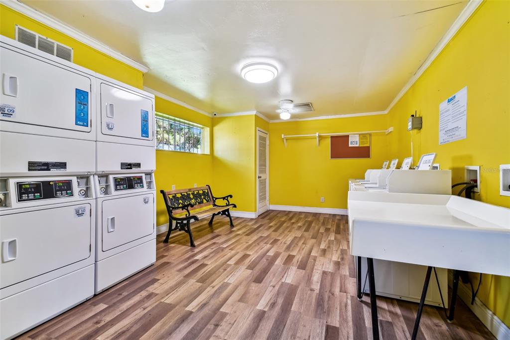 Shared laundry room with commercial machines, bright yellow walls, and a bench by the window.