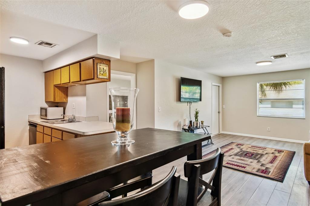 Open-plan kitchen and living area with wood cabinetry, a dark dining table, and a patterned rug.
