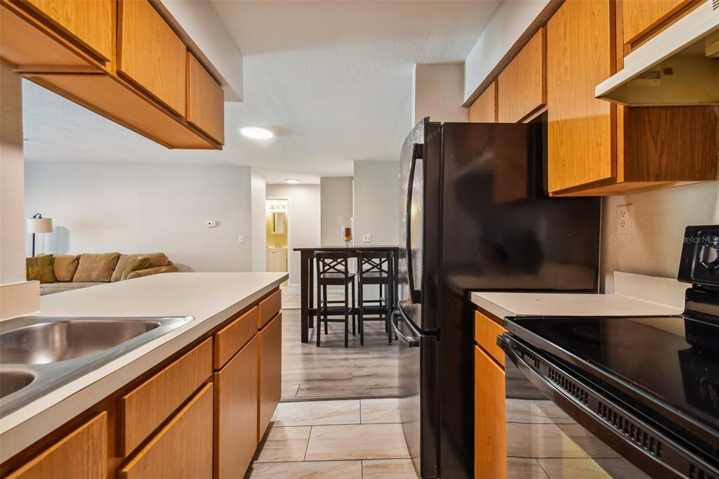 Kitchen with warm wood cabinets and black appliances, opening onto a dining area and living room.