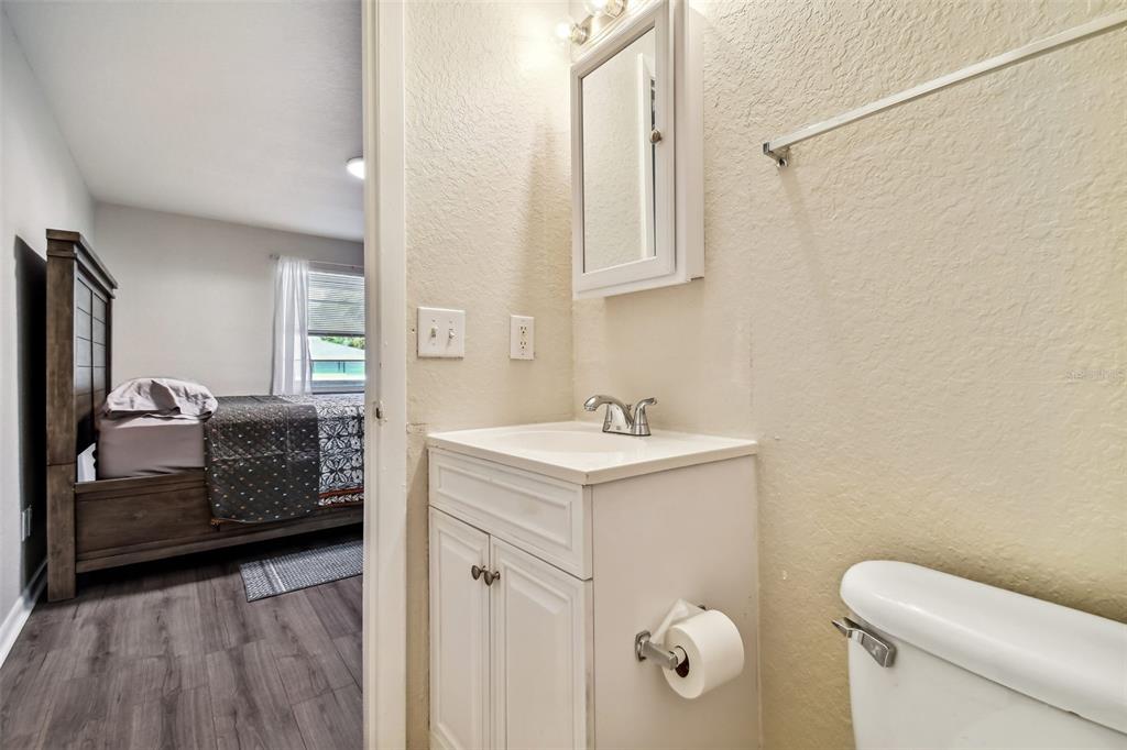 Bathroom vanity and toilet beside an open doorway to a furnished bedroom.