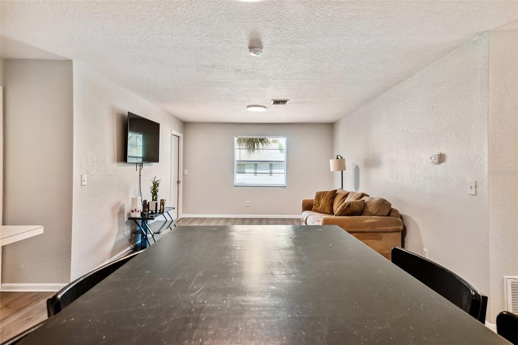 Dining and living area with a large dark table, brown sectional sofa, and wall-mounted television.