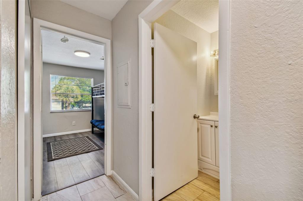 Hallway with open doors to a bathroom vanity and a bedroom with a window and bunk bed.