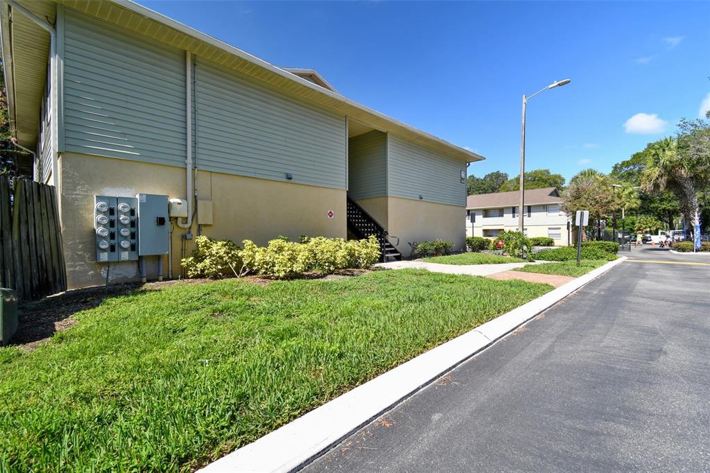Two-story condominium exterior with pale blue siding, utility meters, shrubs, and a driveway.