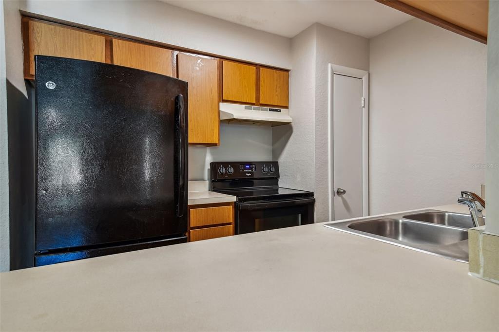 Kitchen with honey-colored wood cabinets, black appliances, and a stainless steel double-basin sink.