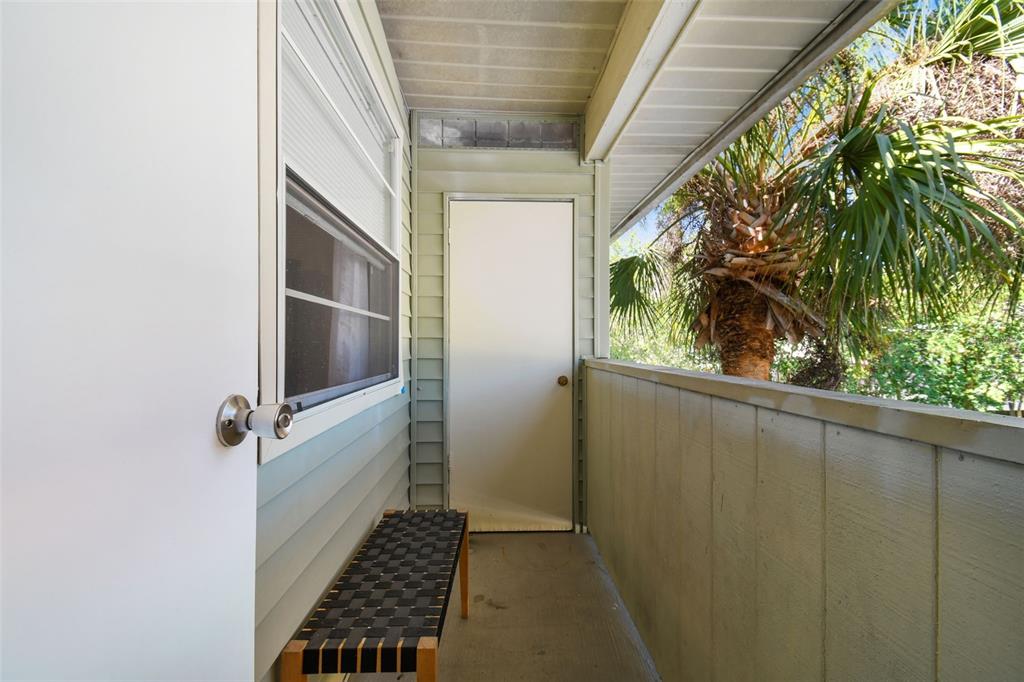 Covered porch with a woven bench and palm trees beyond the railing.
