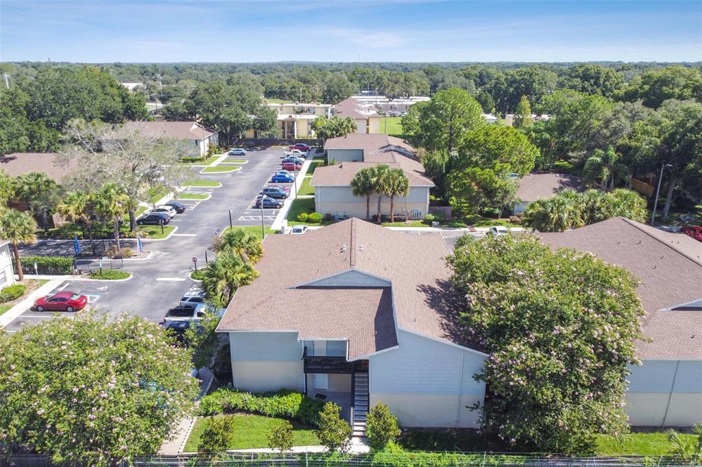 Aerial view of a condominium building beside a parking lot and mature trees.