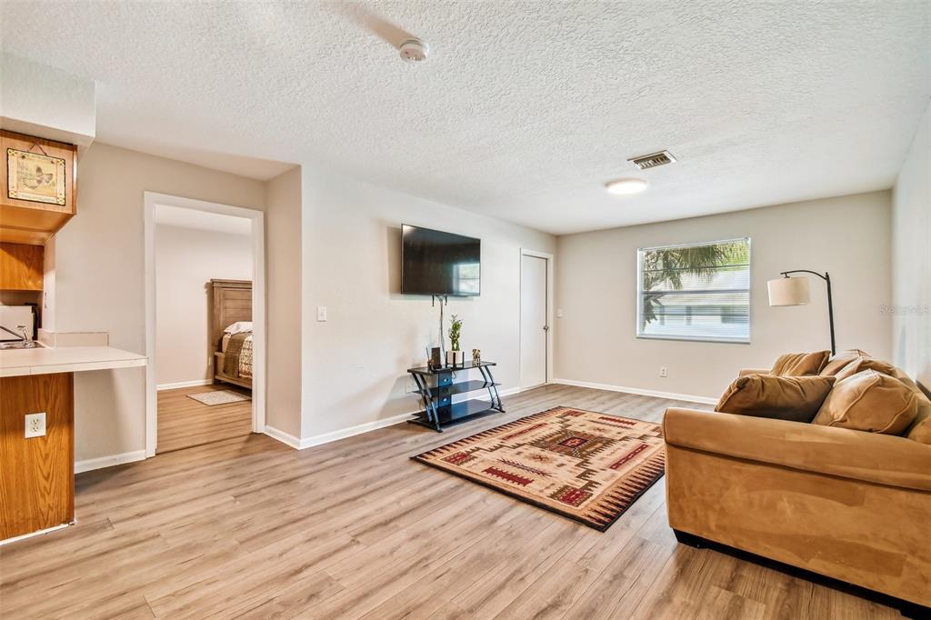 Living room with tan sectional, patterned rug, wall-mounted TV, and light wood-look floors.