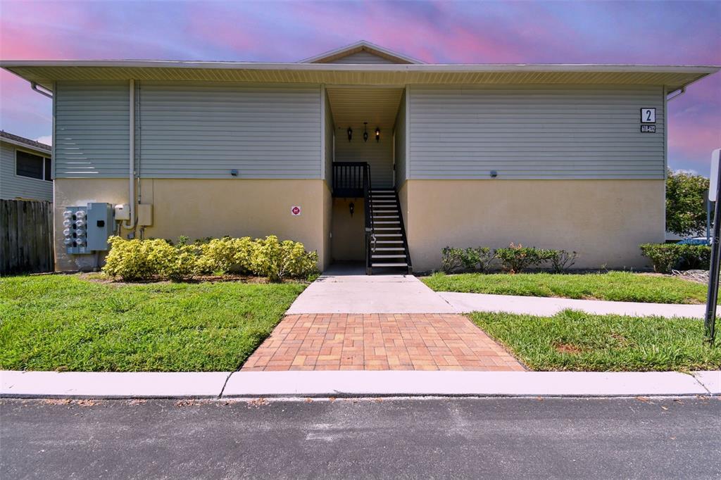Residential building with a recessed central staircase, brick-paver walkway, and landscaped lawn.