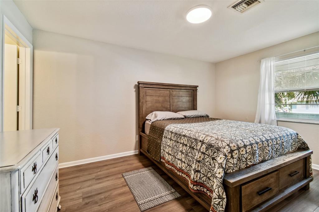 Bedroom with a wooden bed, patterned quilt, white dresser, and window with blinds.