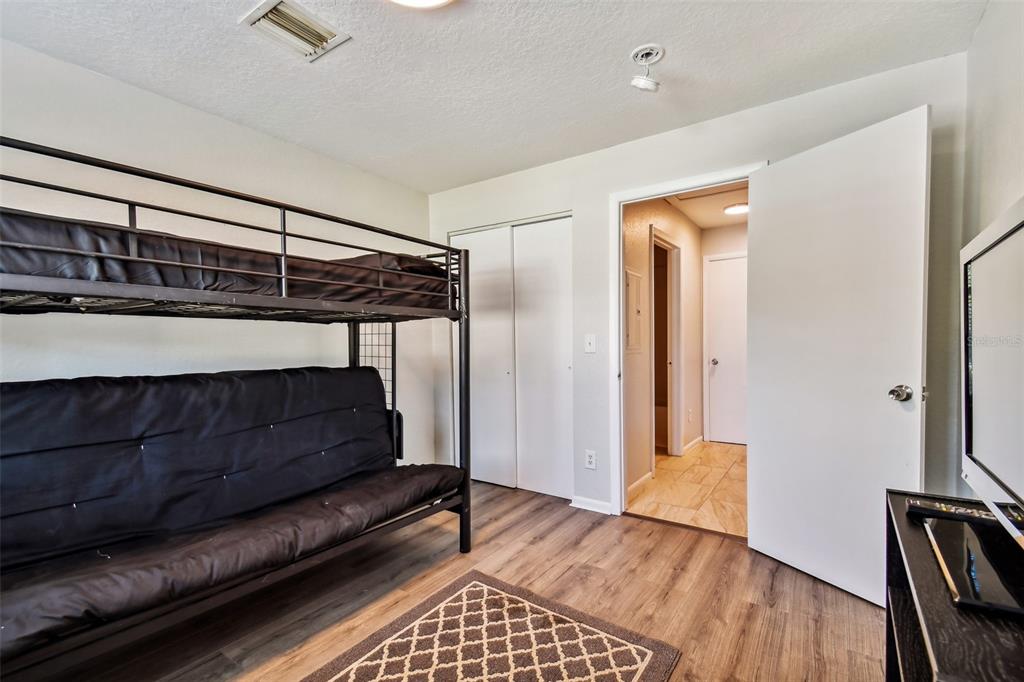 Bedroom with a black metal bunk bed, futon, wood-look flooring, and patterned rug.