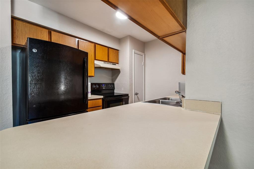 Kitchen with honey-toned cabinets, black appliances, and a large breakfast bar with a double sink.