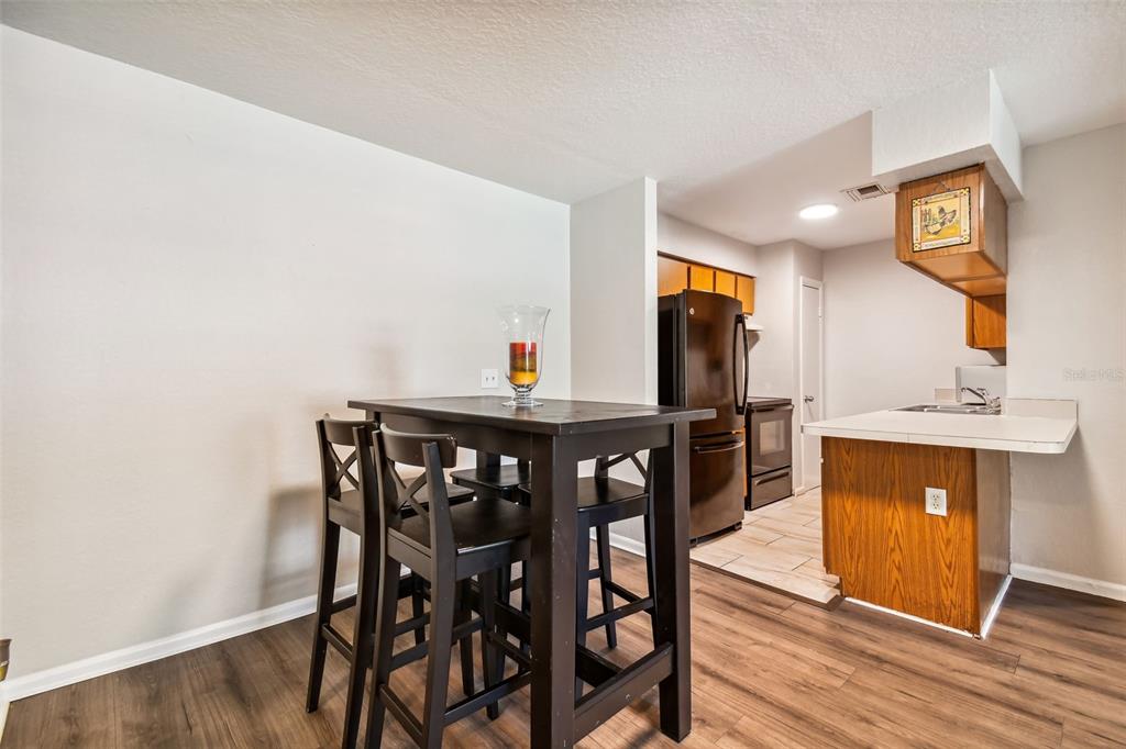 Dining area with a dark table and chairs beside a kitchen with wood cabinets and dark appliances.
