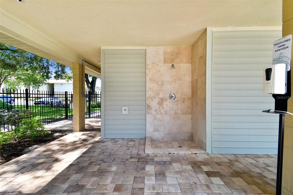 Covered outdoor shower with stone-tile walls, paver flooring, and louvered privacy panels.