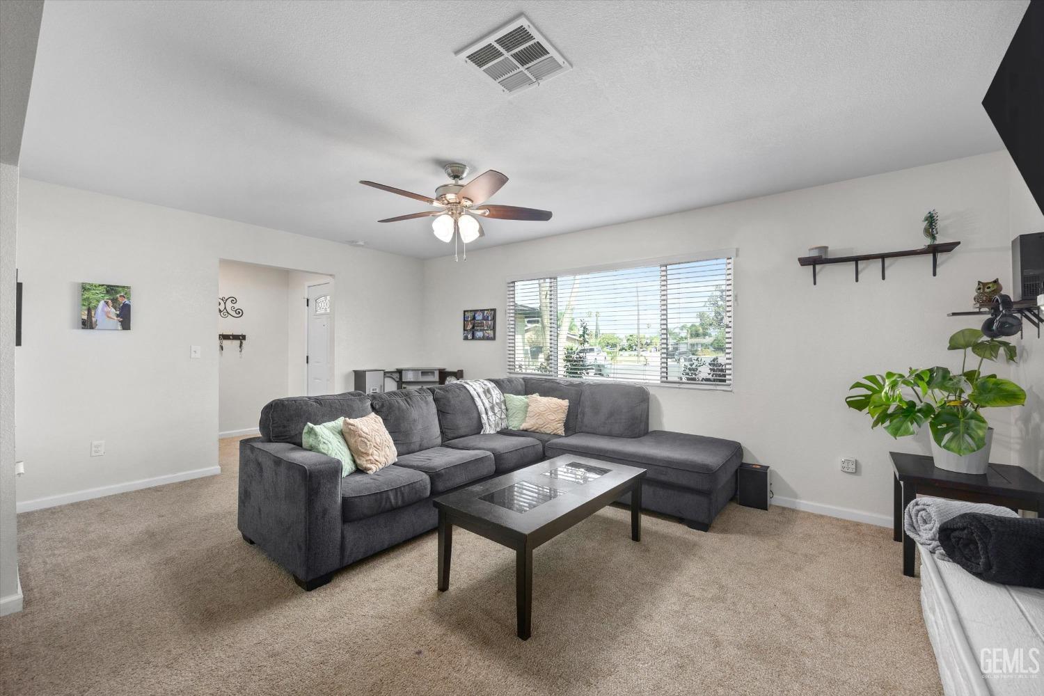 Living room with a gray sectional, glass-top coffee table, and wide window with blinds.