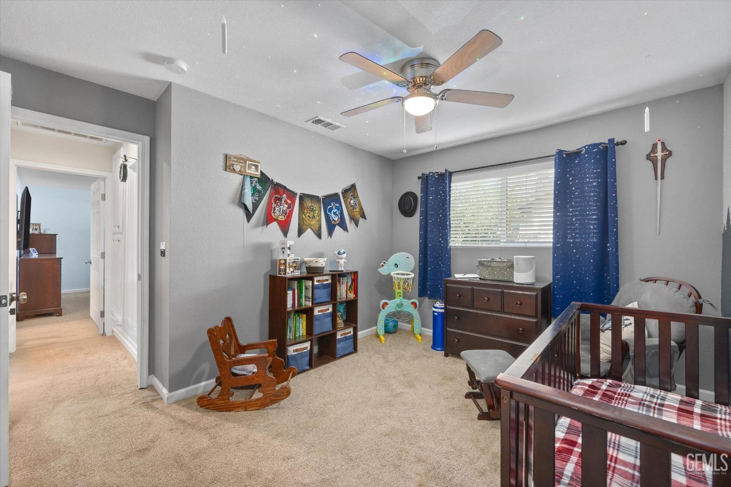 Furnished nursery with a dark wood crib, blue starry curtains, and a ceiling fan.