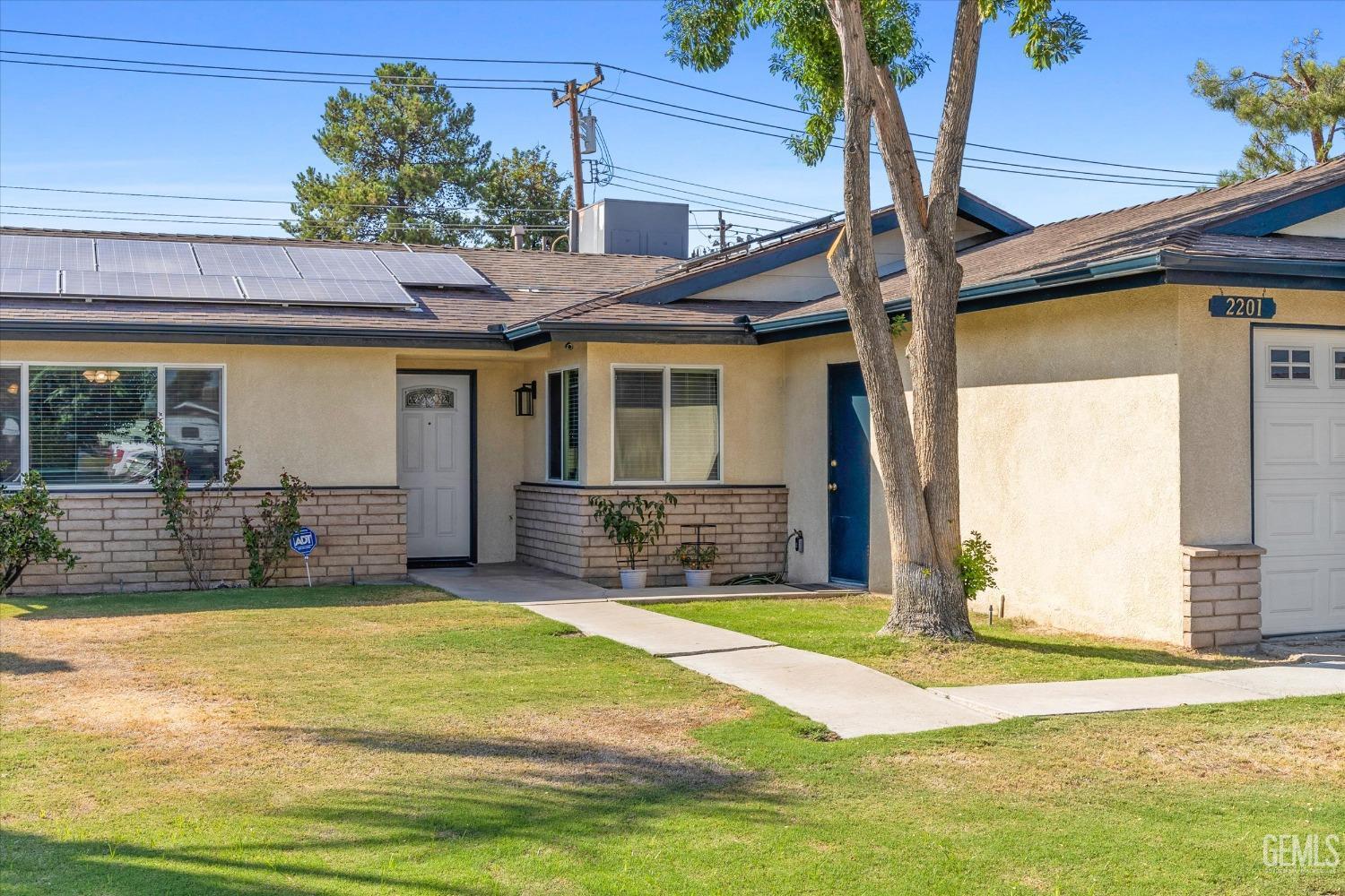 Single-story stucco home with rooftop solar panels, a blue entry door, and a front lawn.
