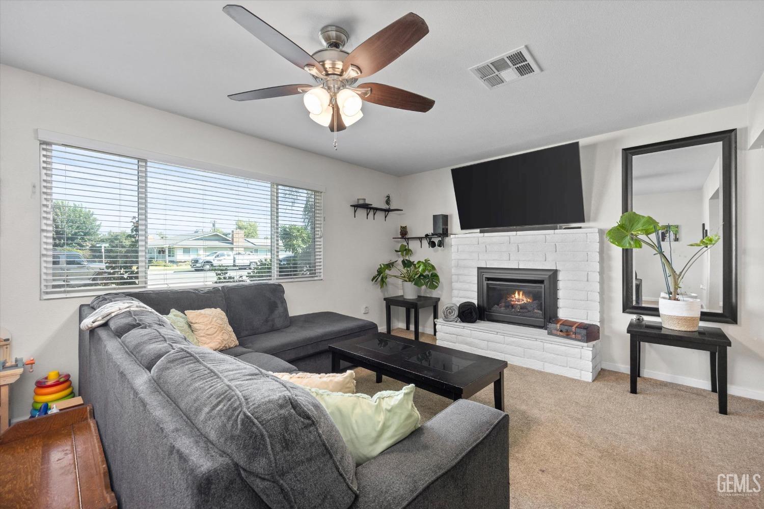 Living room with a gray sectional, white brick fireplace, and large window with blinds.