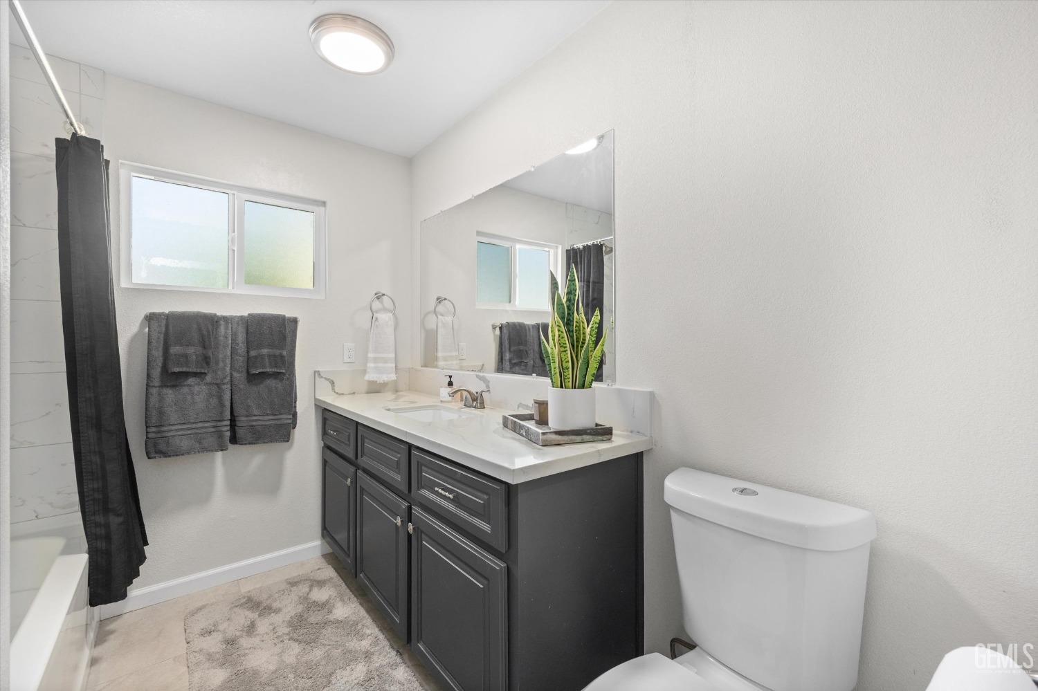 Bathroom with a dark gray vanity, large mirror, frosted window, and potted plant.