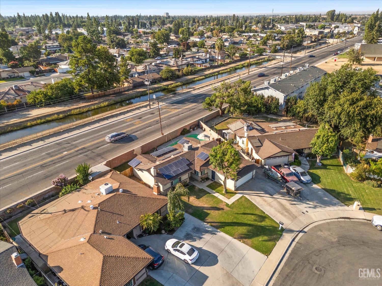 Aerial view of homes beside a canal and busy road, with solar panels visible on several roofs.