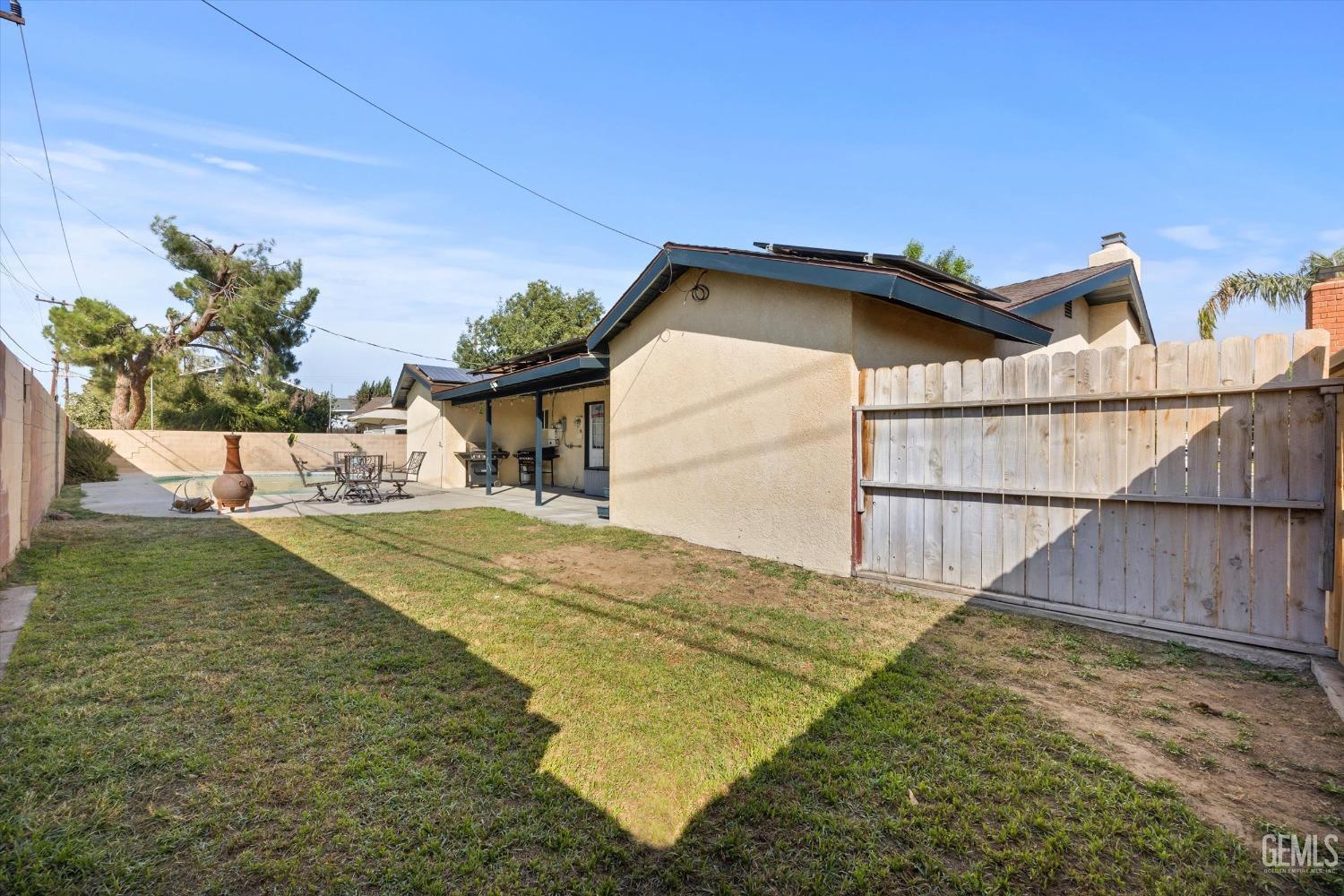 Backyard with a small pool, covered patio, outdoor dining set, and wooden privacy fence.