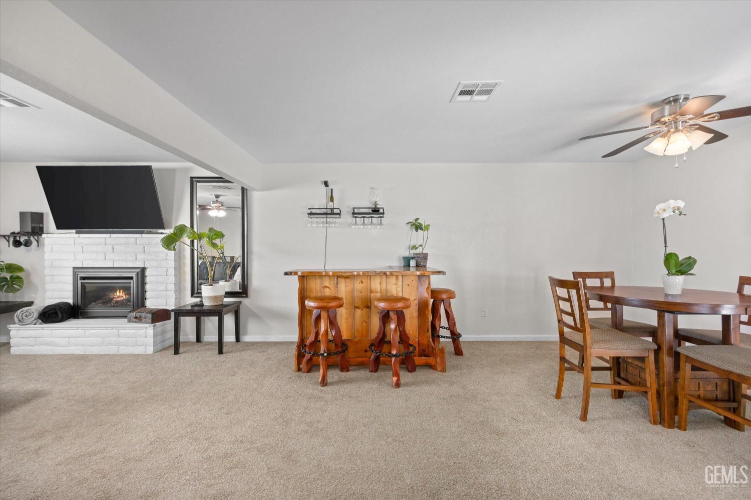 Living and dining room with a white brick fireplace, wooden bar and stools, and a dining table.