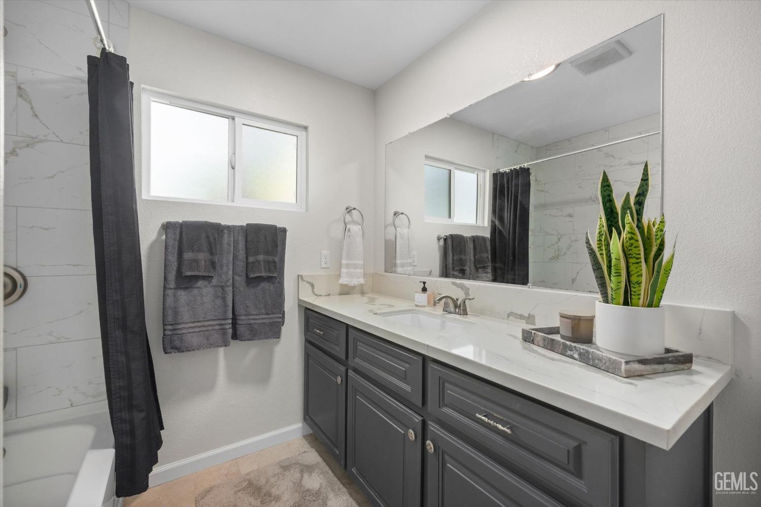 Bathroom with a long dark gray vanity, marble-look countertop, large mirror, and tiled tub-shower.