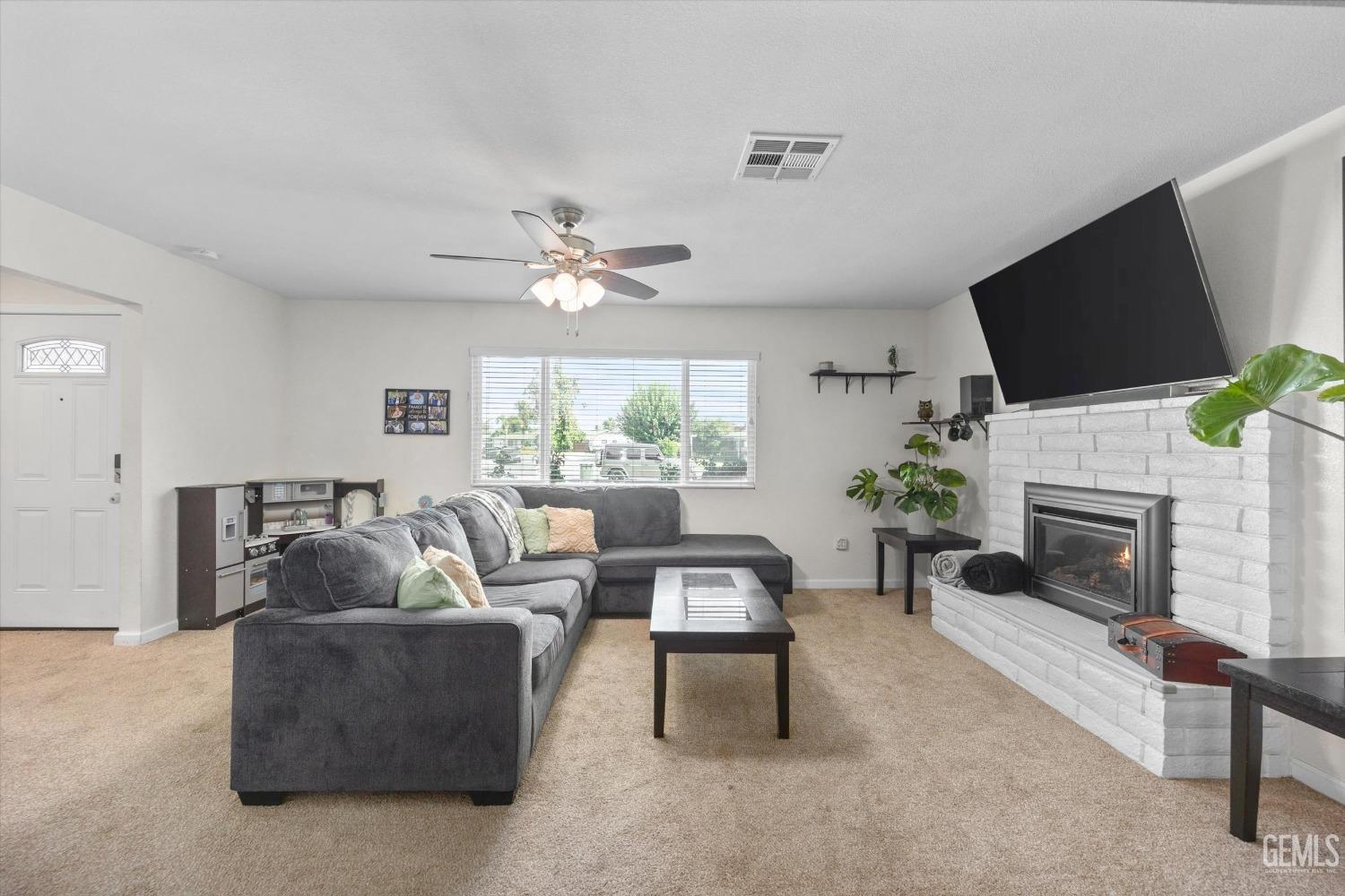 Living room with a gray sectional sofa, white brick fireplace, and large window with blinds.