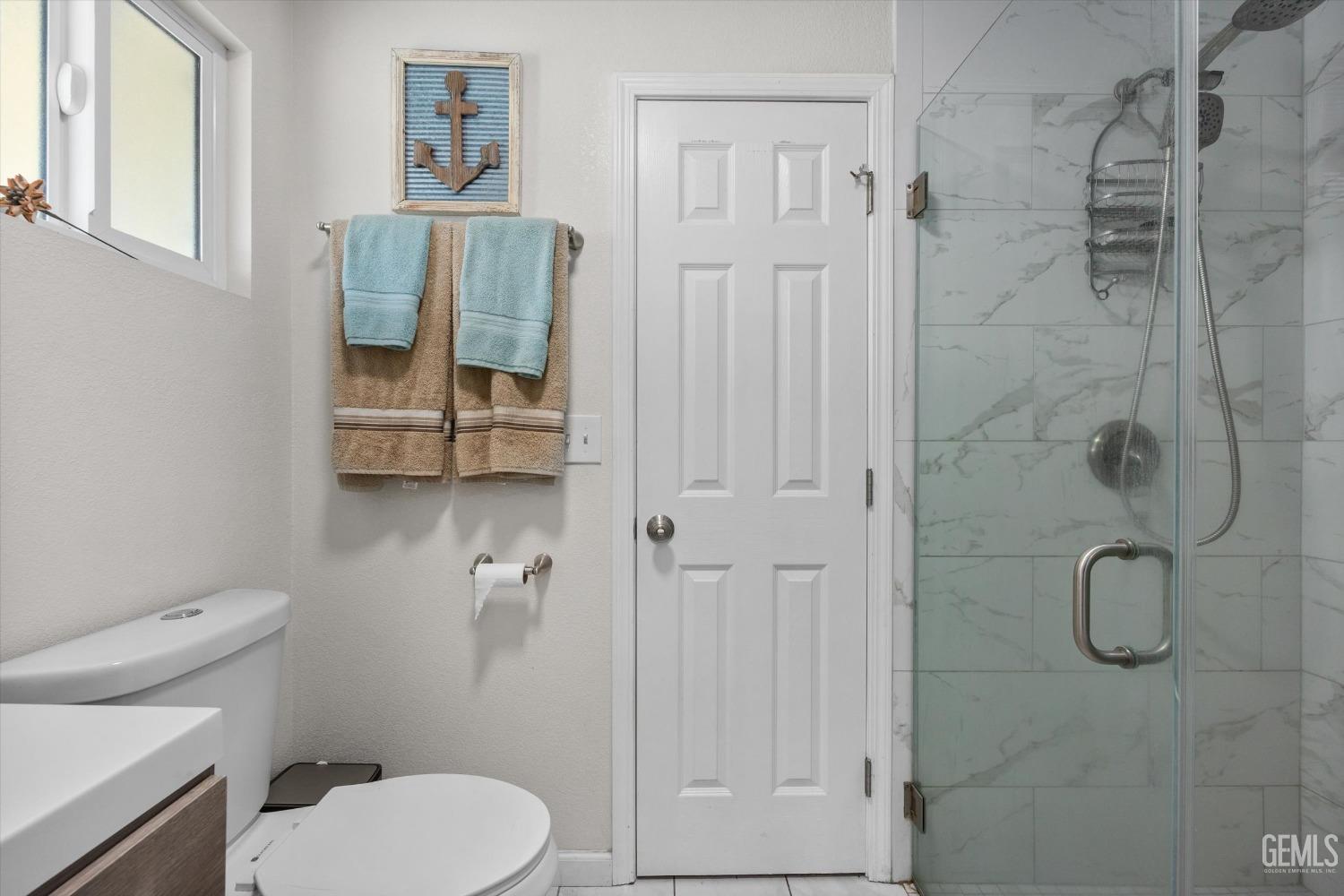 Bathroom with a glass shower, marble-look tile, toilet, and neatly hung towels.