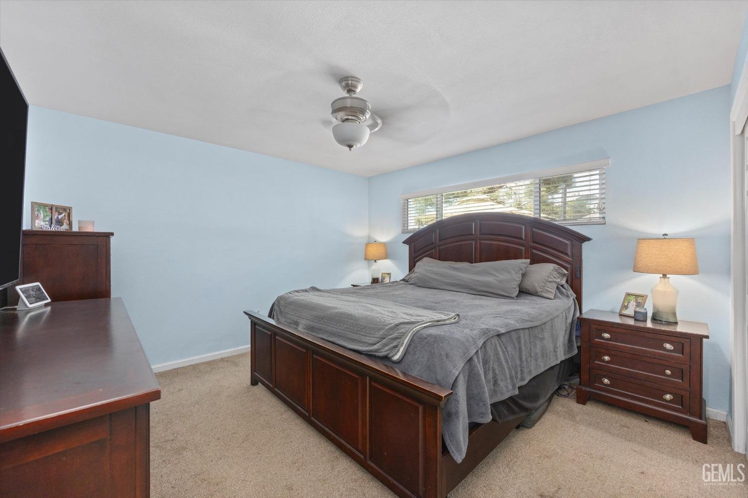Bedroom with a dark wood bed, gray bedding, light blue walls, and a wide window above the headboard.