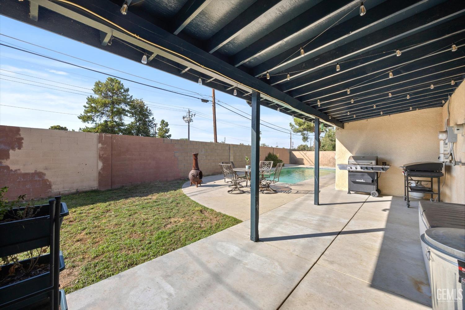 Covered backyard patio with string lights, outdoor seating, grills, and a pool.