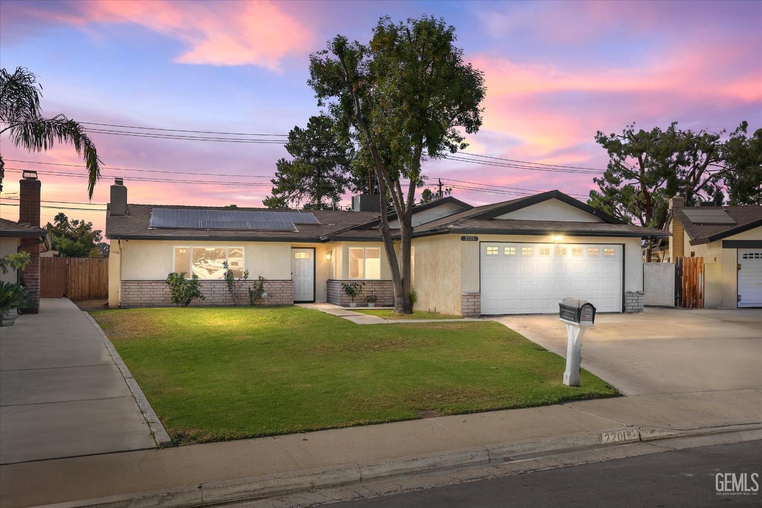 Single-story home with rooftop solar panels, an attached garage, and a broad front lawn at dusk.