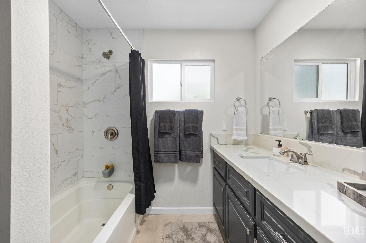 Bathroom with marble-look tub surround, dark shower curtain, and long gray vanity.
