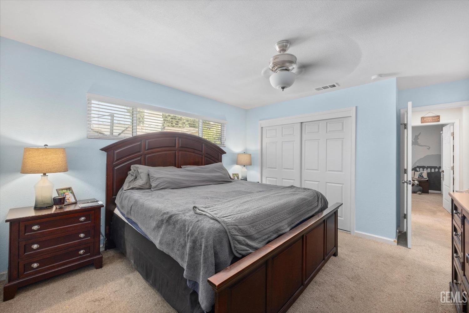 Furnished bedroom with a dark wood bed, gray bedding, pale blue walls, and white closet doors.