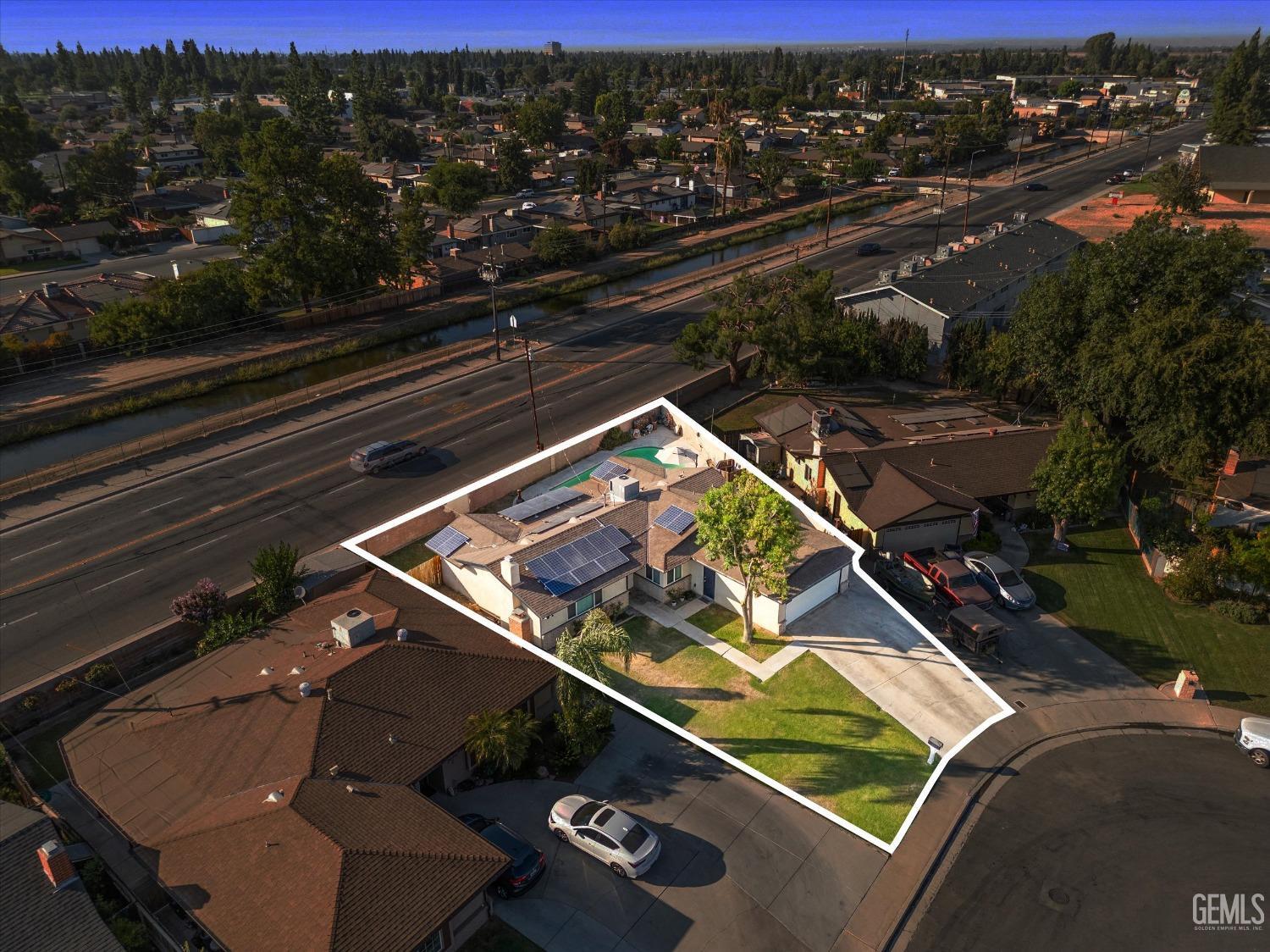 Aerial view of a single-story home with rooftop solar panels and a white outline marking its lot.