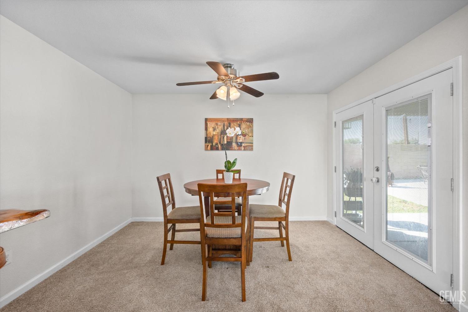 Dining area with a round wooden table, ceiling fan, and French doors to the patio.