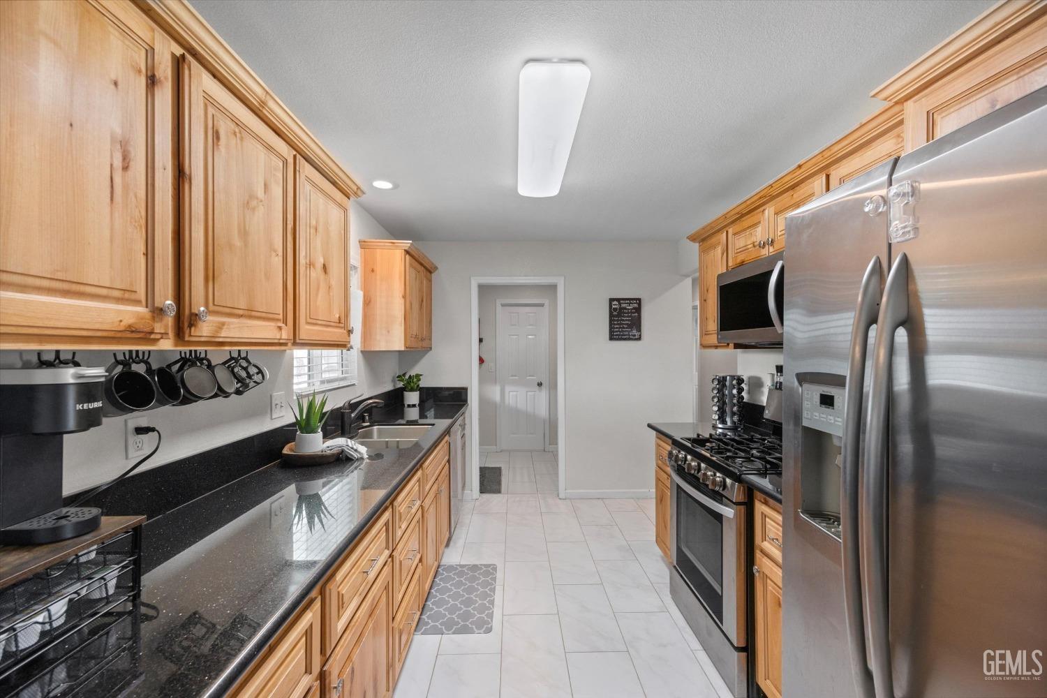 Galley kitchen with honey-colored cabinets, black countertops, and stainless steel appliances.