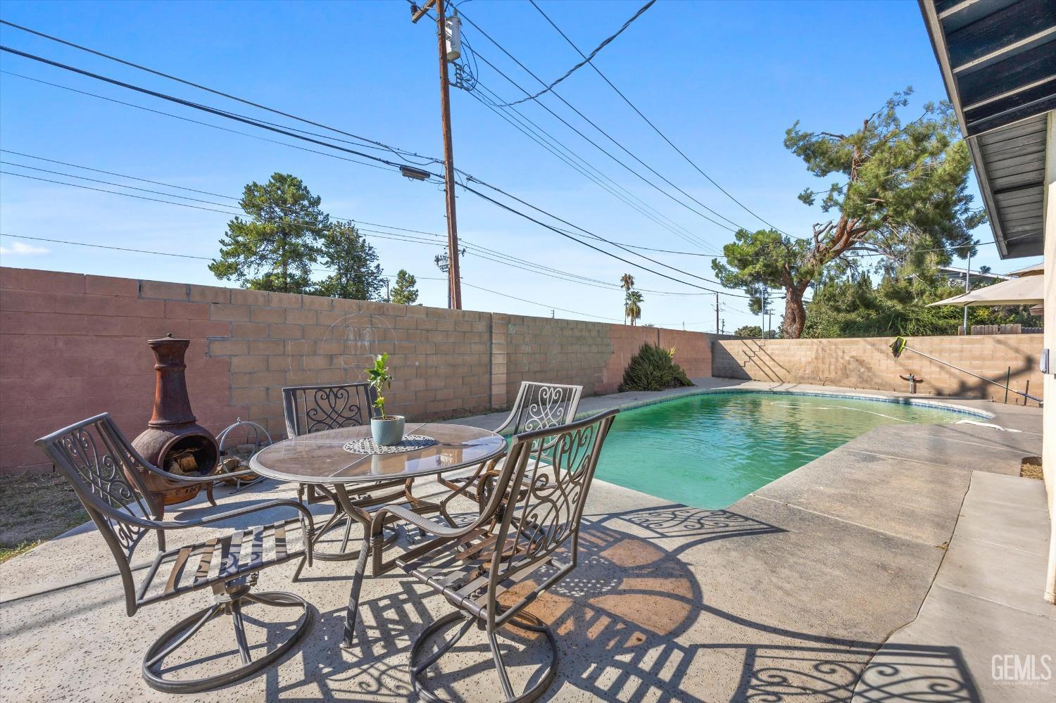 Backyard swimming pool beside a patio dining set and outdoor fireplace.