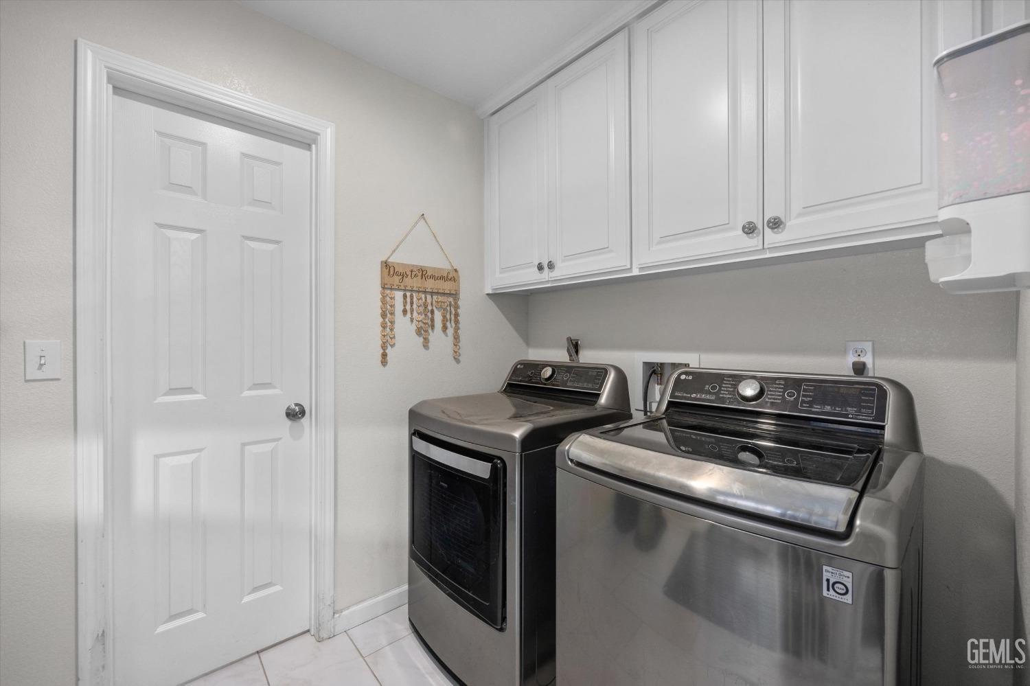 Laundry room with a front-loading washer and dryer beneath white cabinets.