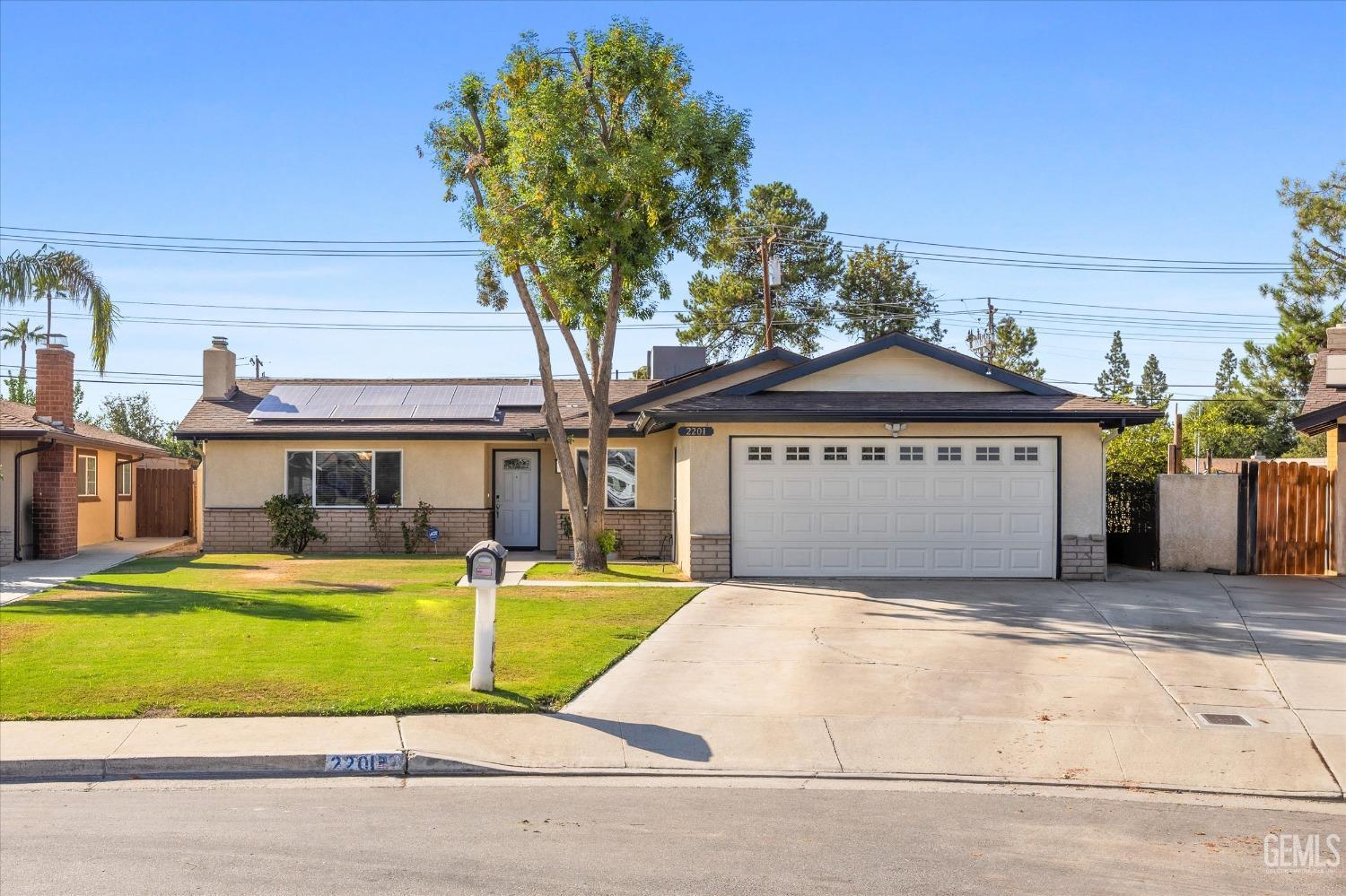 Single-story house with solar panels, a two-car garage, and a large front-yard tree.