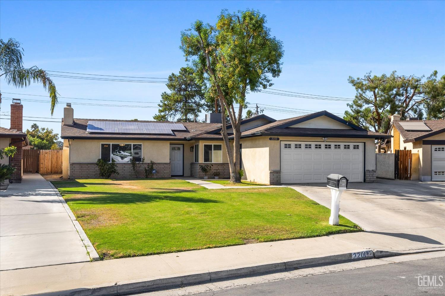 Single-story house with rooftop solar panels, a two-car garage, and a large front lawn.