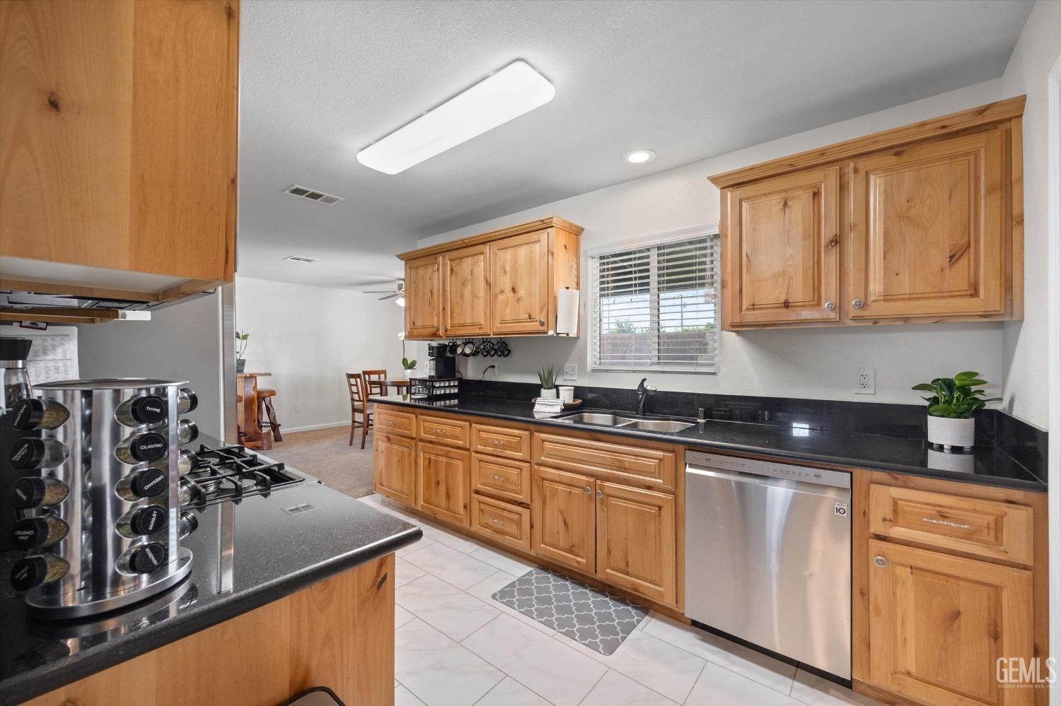 Kitchen with honey-colored wood cabinets, black countertops, and a stainless steel dishwasher.