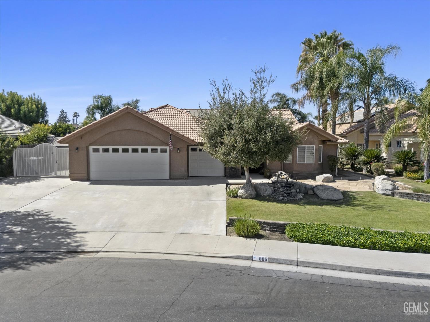 Single-story stucco home with tile roof, two garage doors, and landscaped front yard.